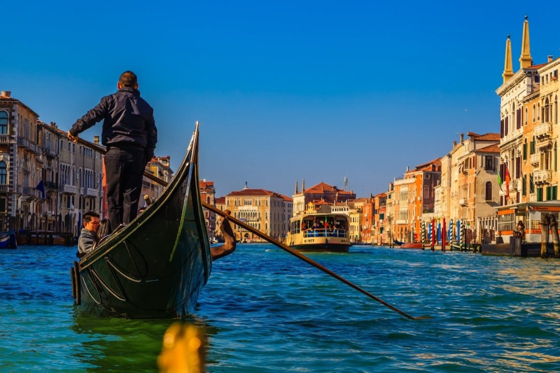 Gondoleiro transporta turistas pelo Canal Grande num dia ensolarado.